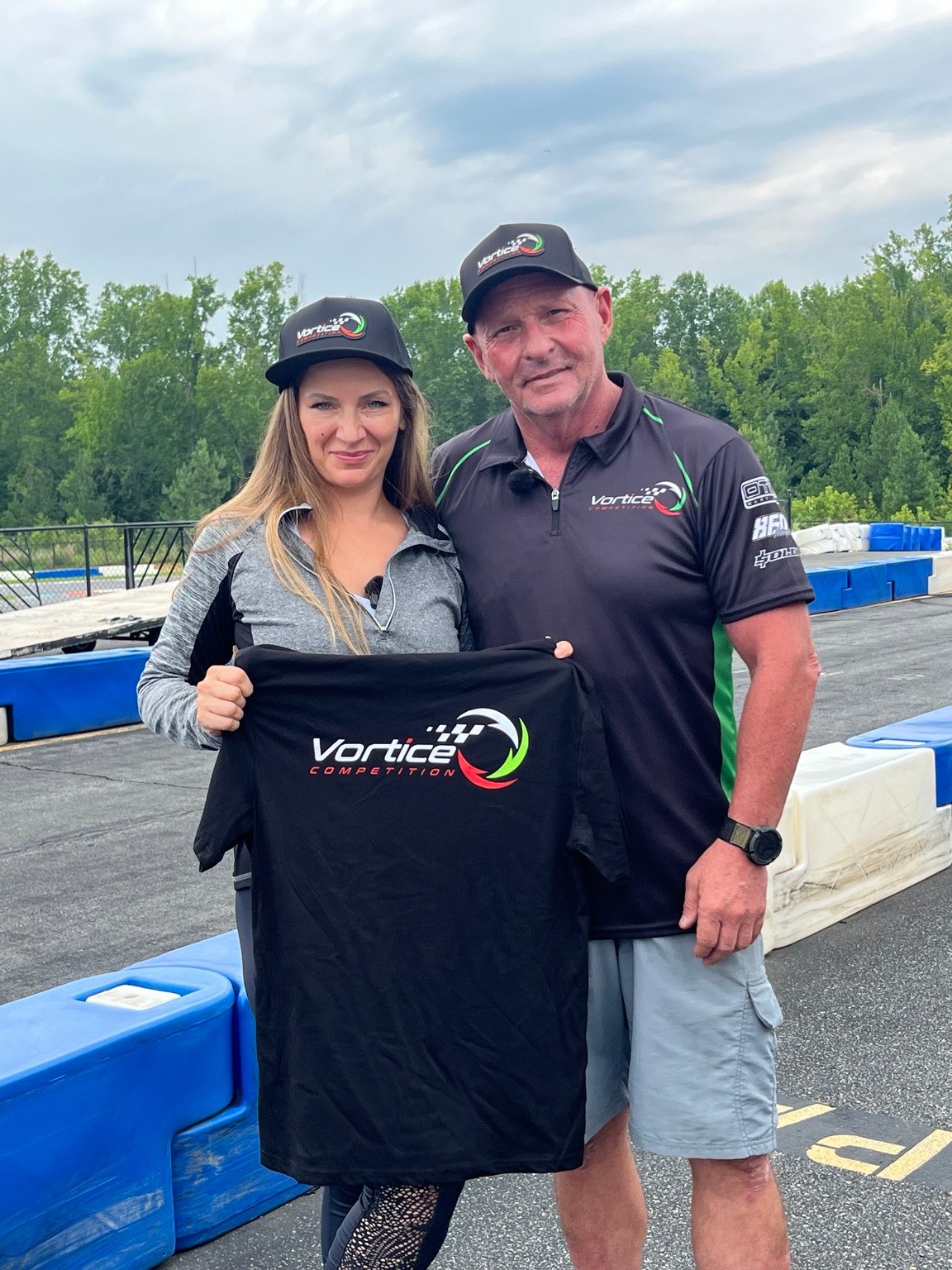 Elena and Sergio standing at the track holding a Vortice Competition T-shirt